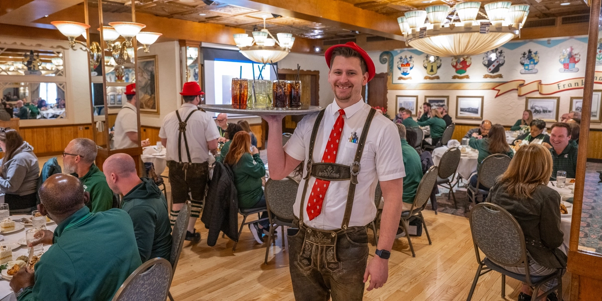 A waiter in a classic German outfit holds sodas on a tray