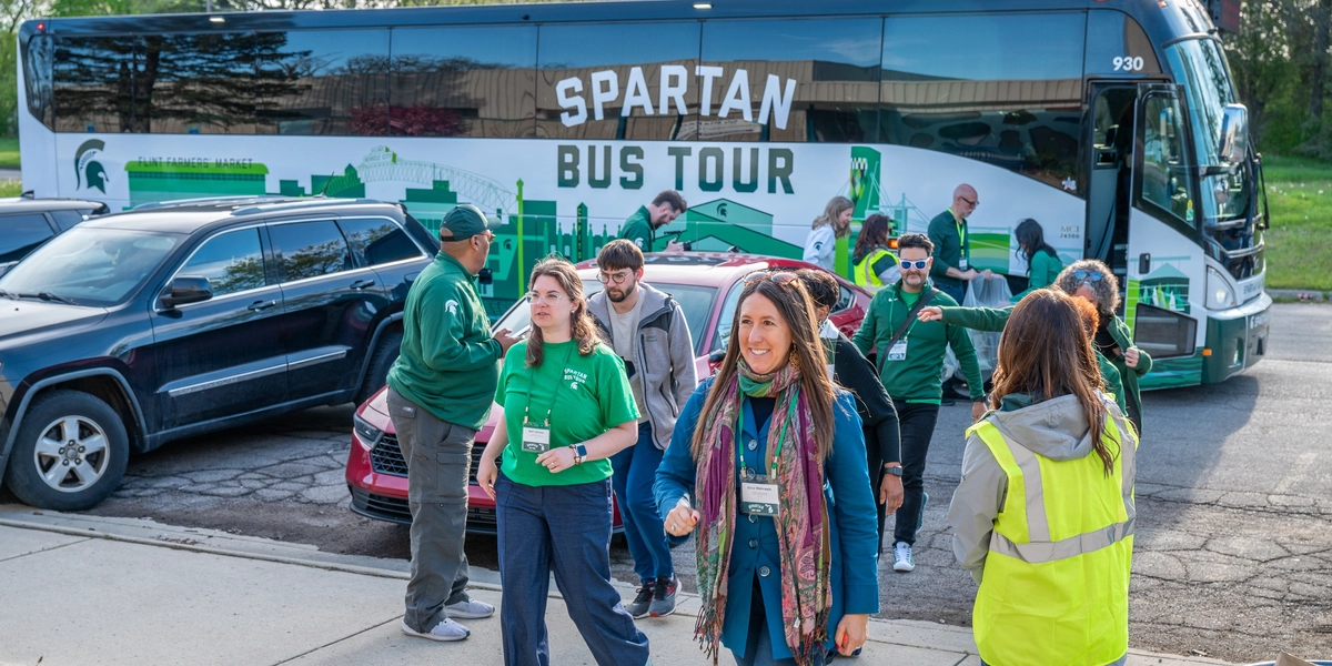 A group of people walks off a bus with a large SPARTAN BUS TOUR logo