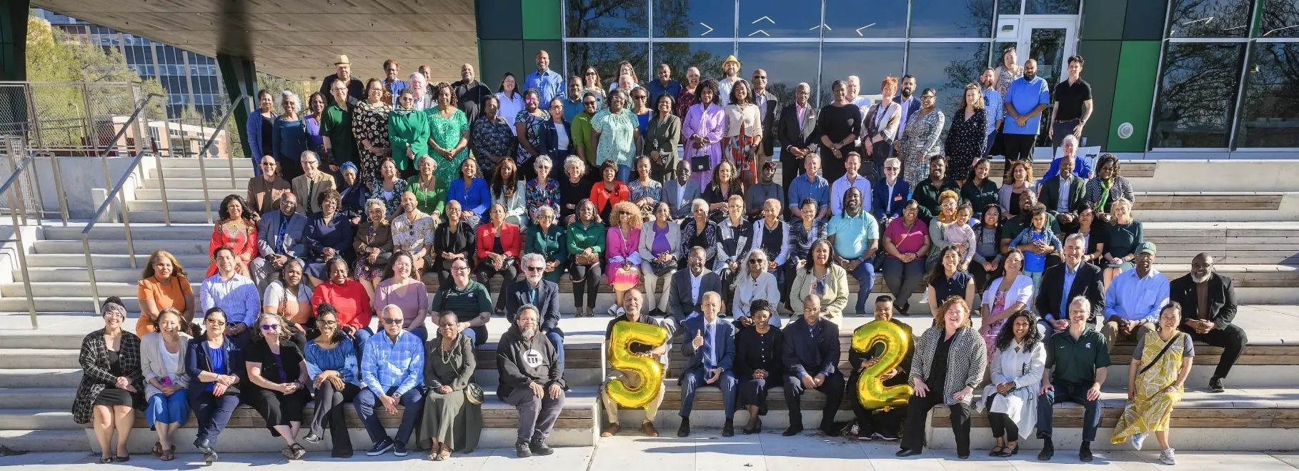 Large group of people sitting on steps, the number 52 is balloon lettering is held in the front