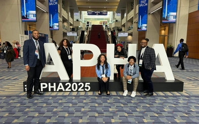 Flint Public Health Youth Academy students pose for a photo in a convention center in front of a sign for APHA 2025.