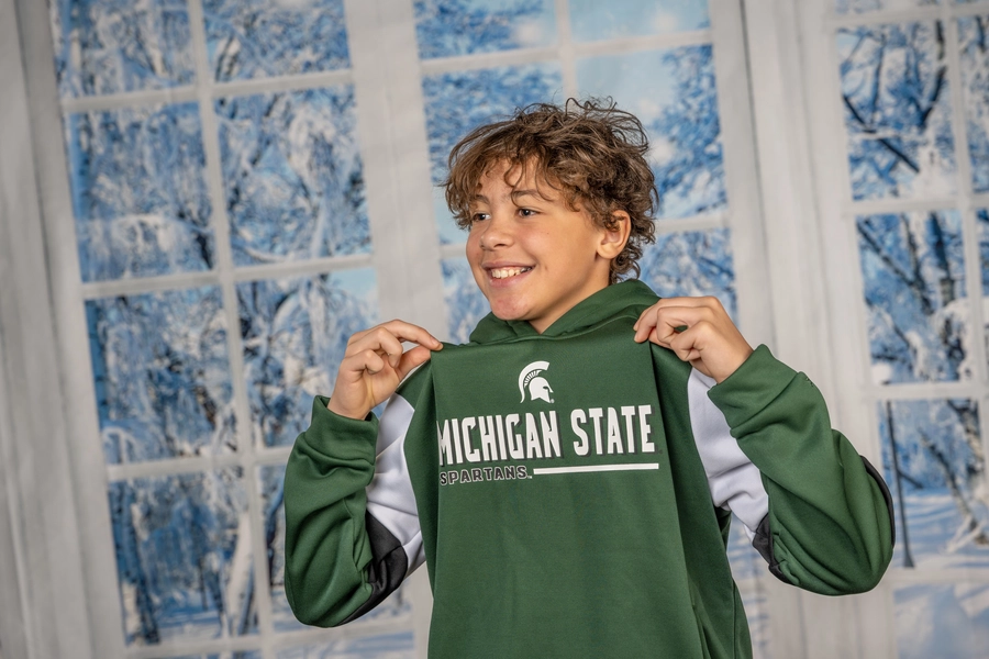 Smiling boy holding up his sweatshirt in front of a winter back drop