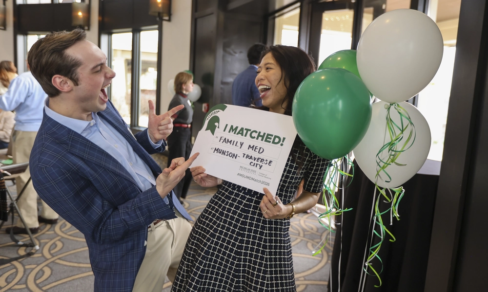 Two medical students celebrating with green and white balloons and a match sign in Grand Rapids.