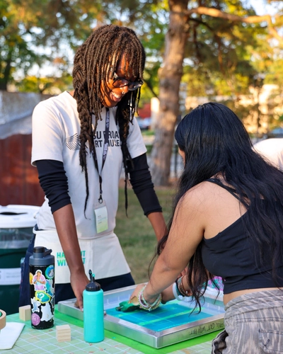 Two students collaborating on a screen printing activity during a campus event located outdoors.