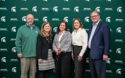 A group of MSU leaders of mixed genders and backgrounds posing together in front of a green Broad College of Business backdrop.