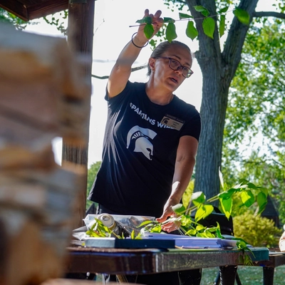 Lindsey Kerr inspecting leaves on a table during an outdoor workshop.