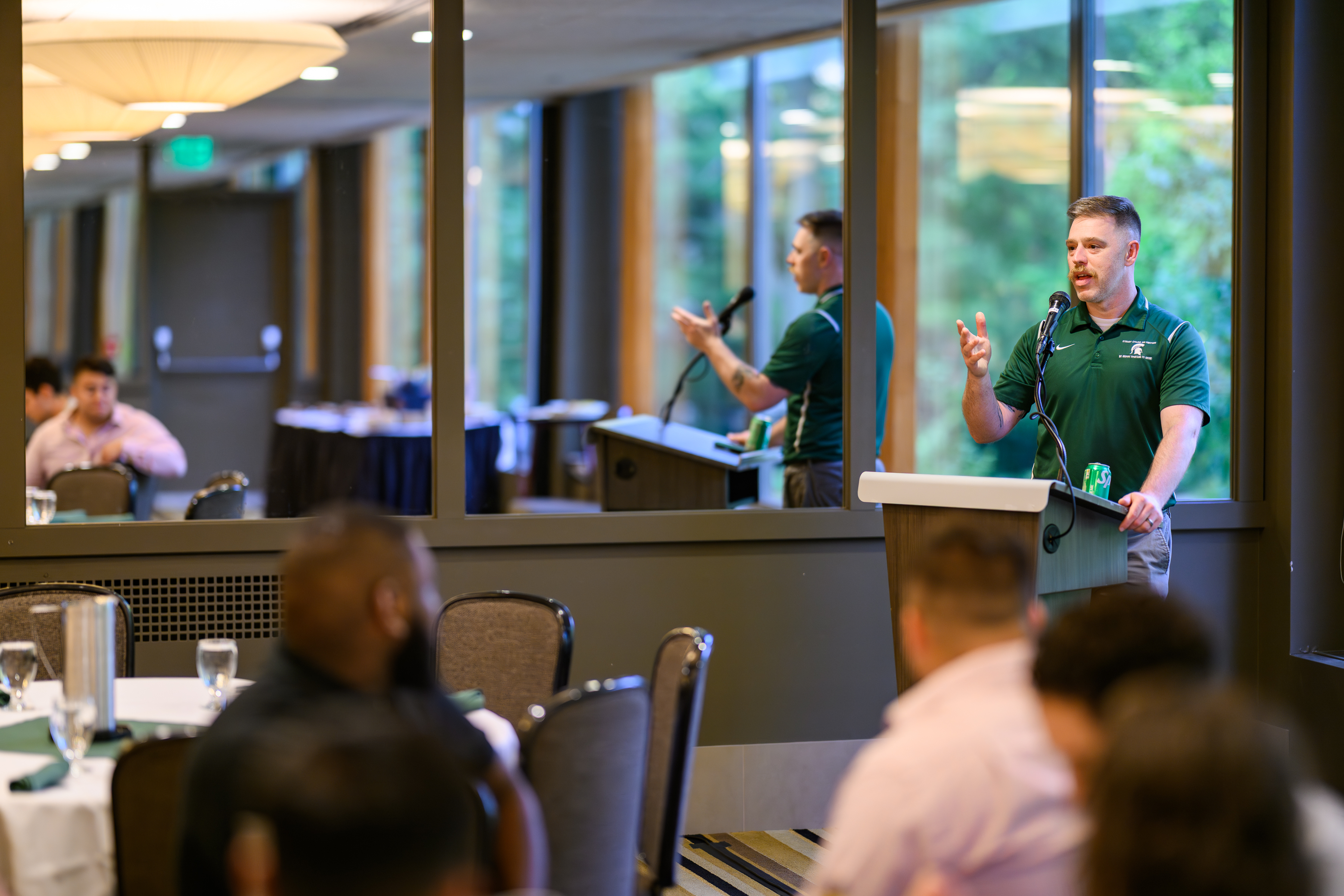 a man in a green polo stands at a podium speaking at a celebration