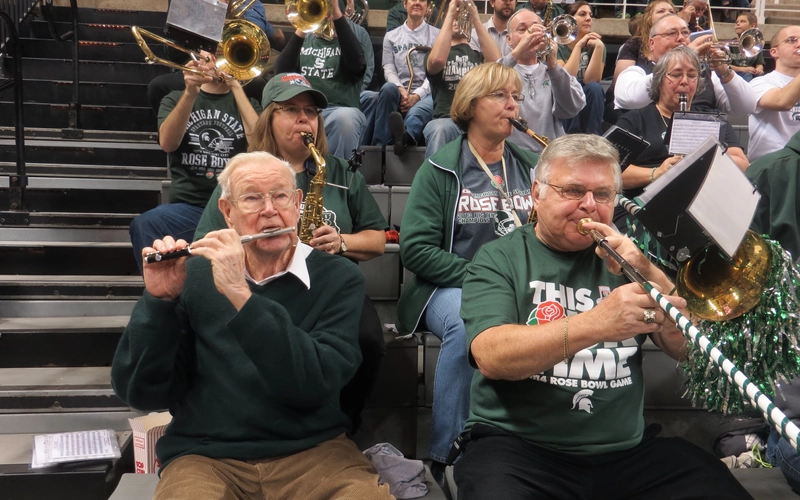Musicians play various instruments while seated on stadium bleachers.