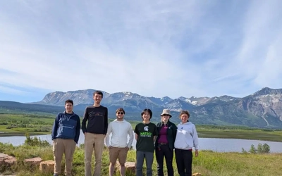 University of Victoria students and Michigan State University students Gabriel Carcereri, Charles McBride and alumni Keyi Cheng standing together in front of mountains in Waterton National Park, Alberta.