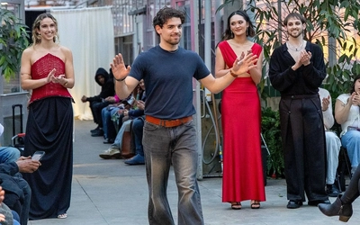 Fernando Caccia stands on the runway next to three models wearing his designs as the crowd claps.