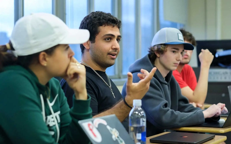 Four students listen and talk during a civil discourse class with laptops sitting on their desks.