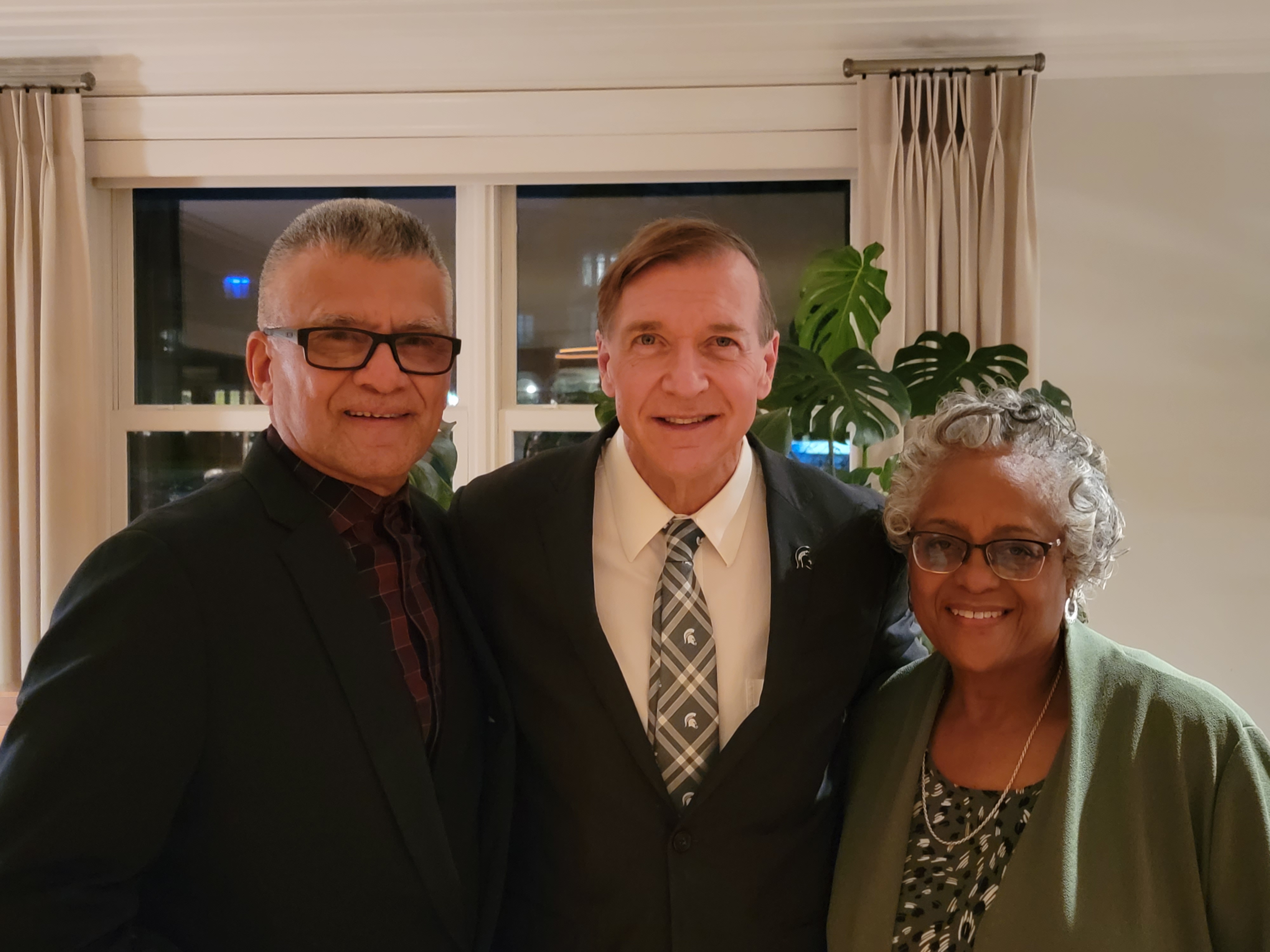 Three people smiling in front of a window