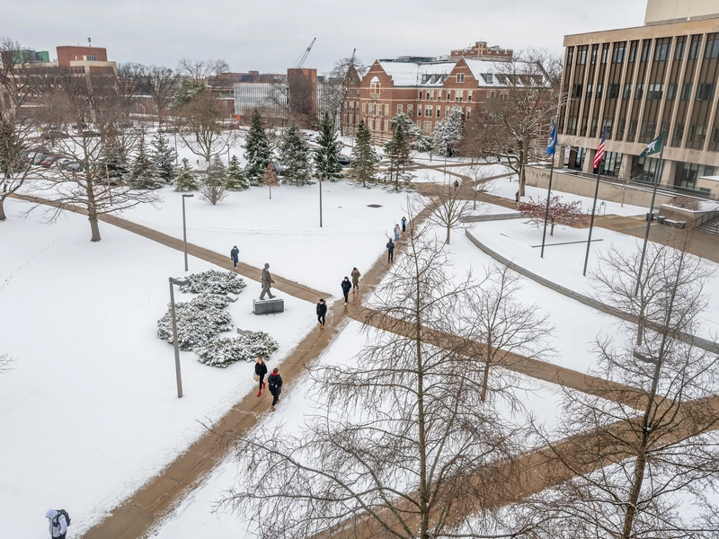 People walking on sidewalks surrounded by snowy grass in front of the Hannah Administration Building.
