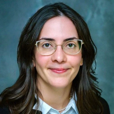 Portrait of Meltem Yucel wearing glasses, a light blue shirt and dark blazer.