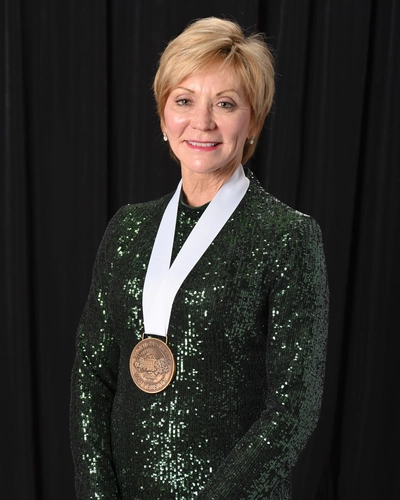 Bonnie Larson smiles while wearing a green sequined dress and an MSU Alumni Grand Award medallion against a black backdrop.