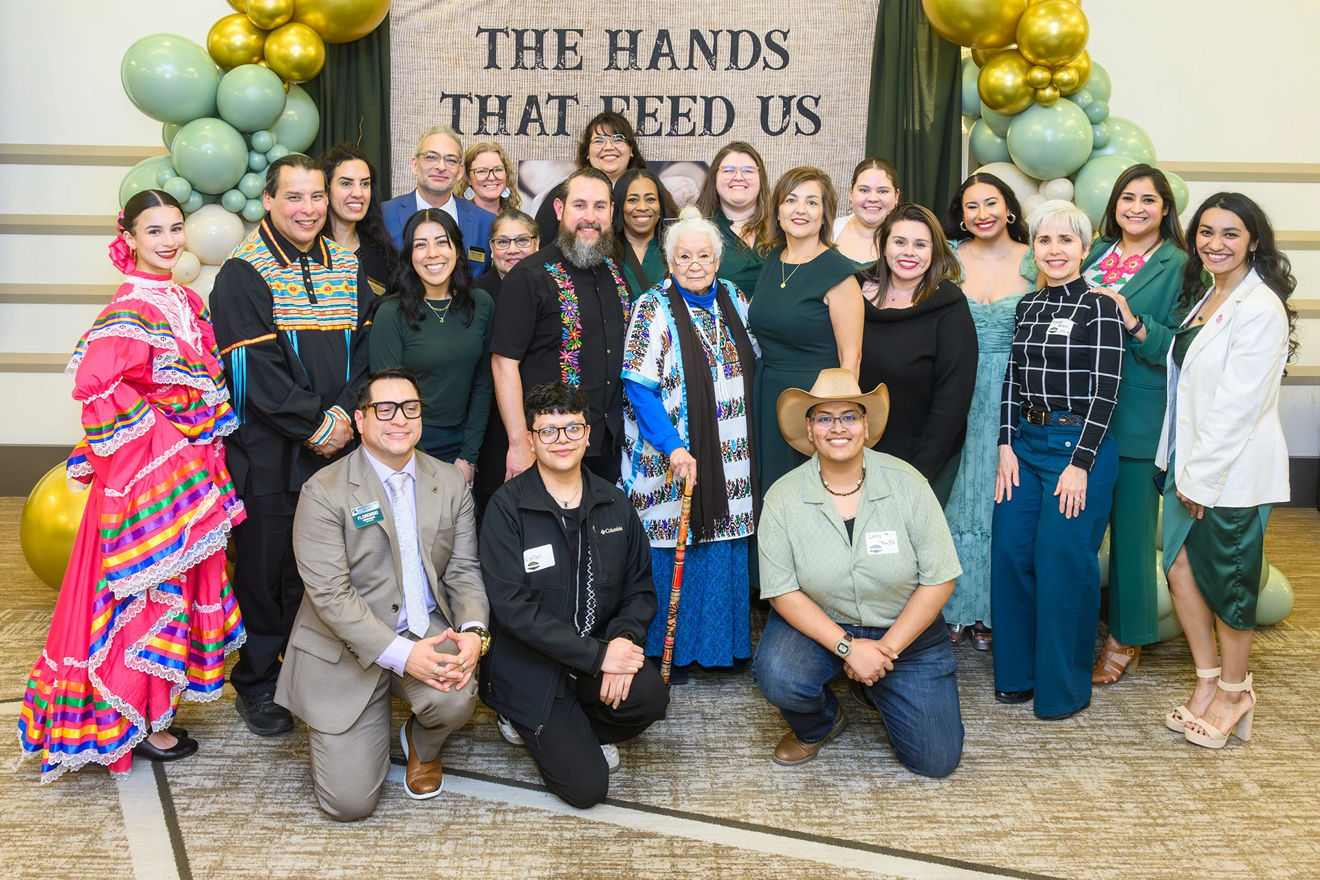 A large group pose in front of a background with the words the hands that feed us