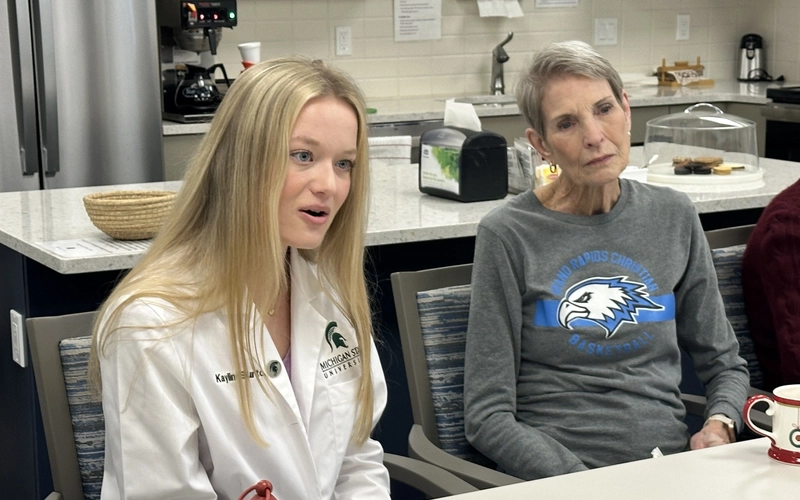 Kaylin Burton speaks while sitting at a table next to a senior Holland Home resident.