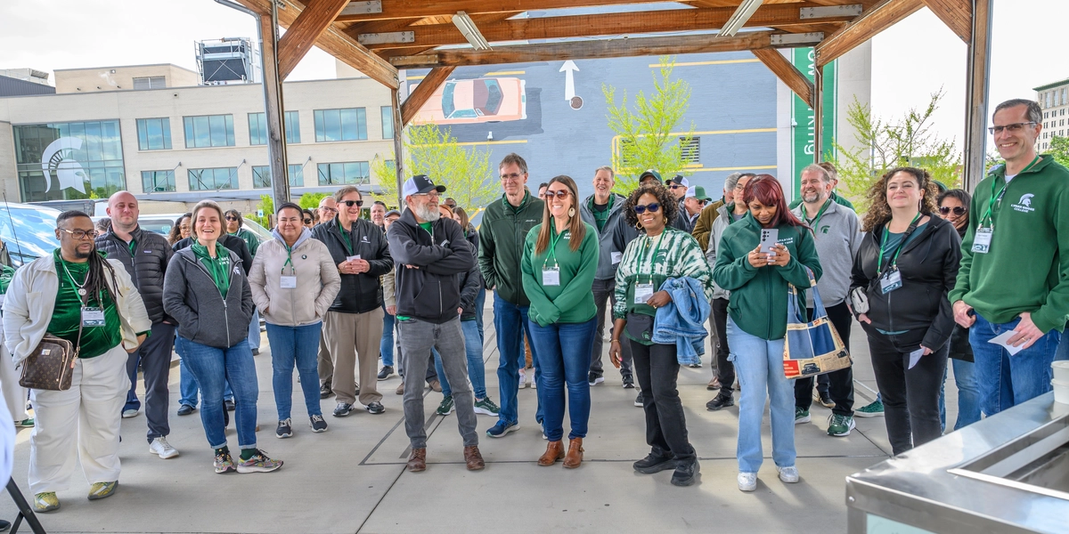 Group of people stand under a pergola at the Flint Farmers