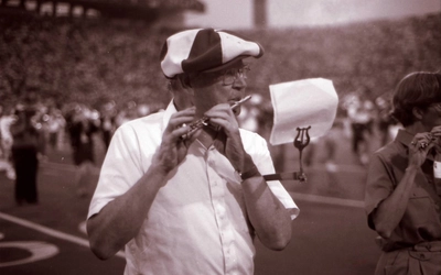 Henry Nelson plays piccolo while where a striped hat during halftime on a football field