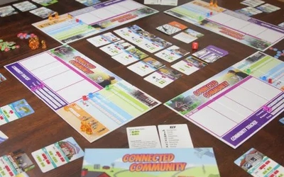 Connected Community board game boards, cards and dice set up on a wooden table.