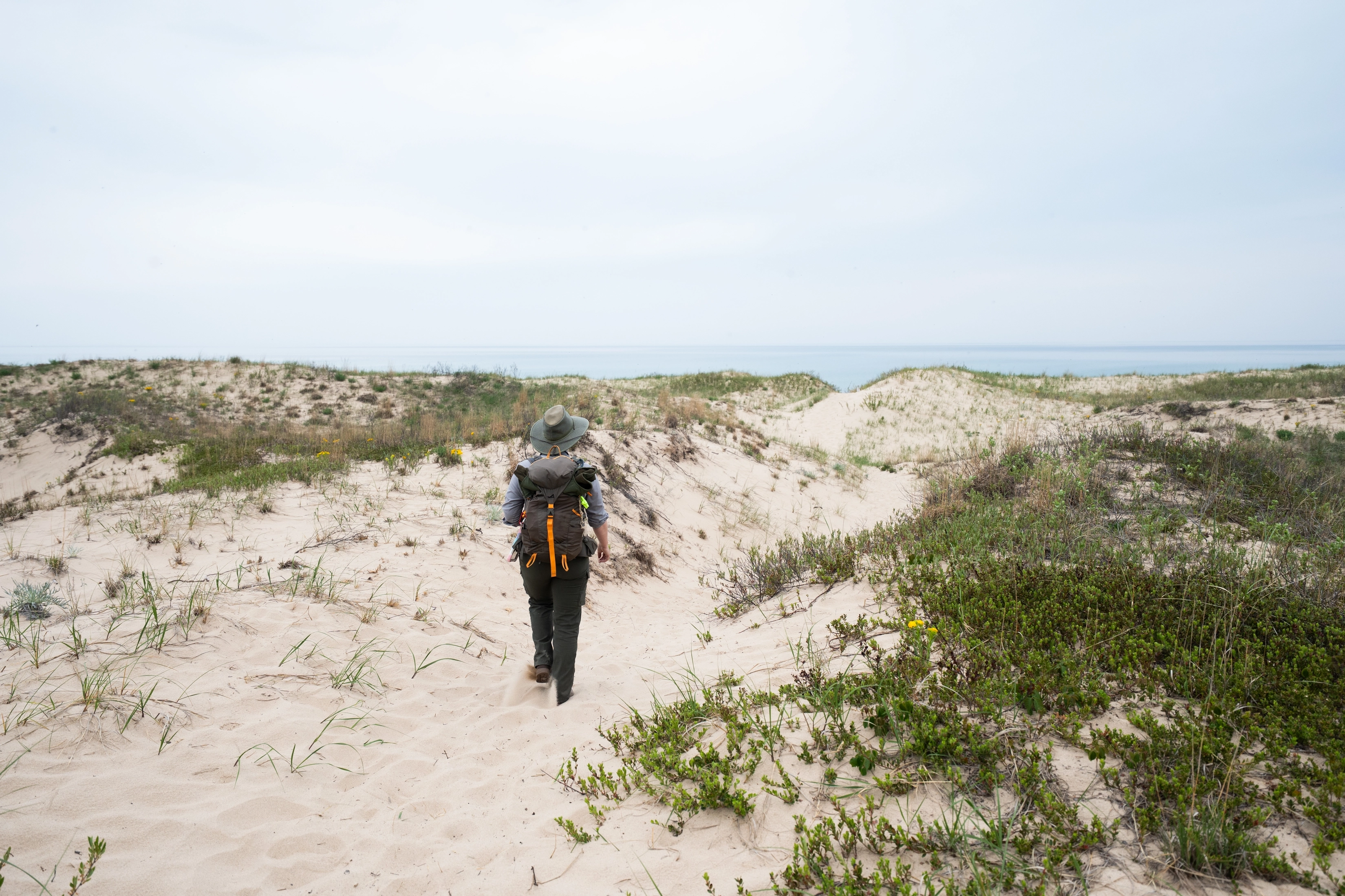 A ranger walks along a sandy dune trail toward Lake Michigan.