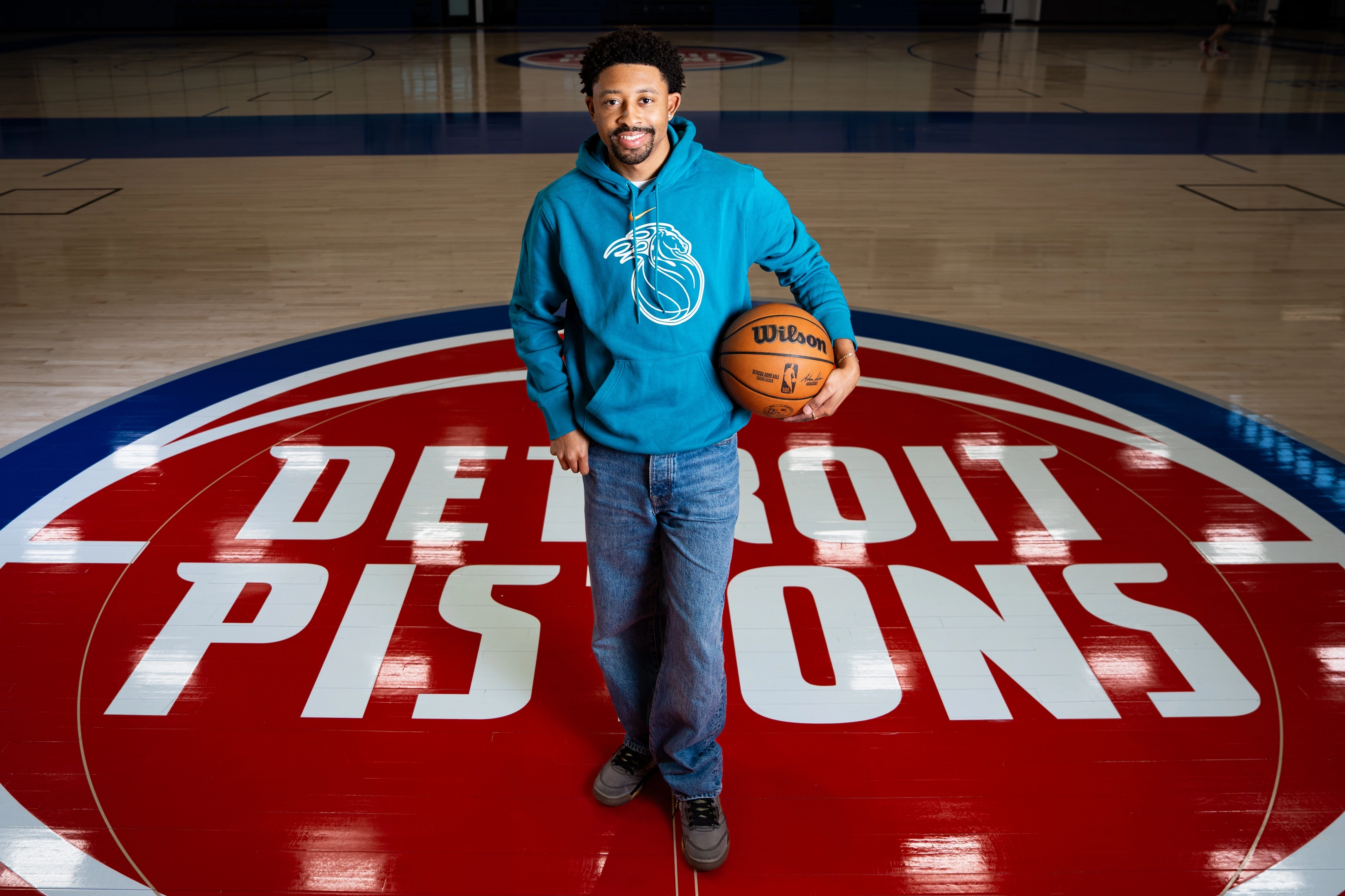 Tamar Davis stands on the Detroit Pistons logo at center court, holding a basketball.