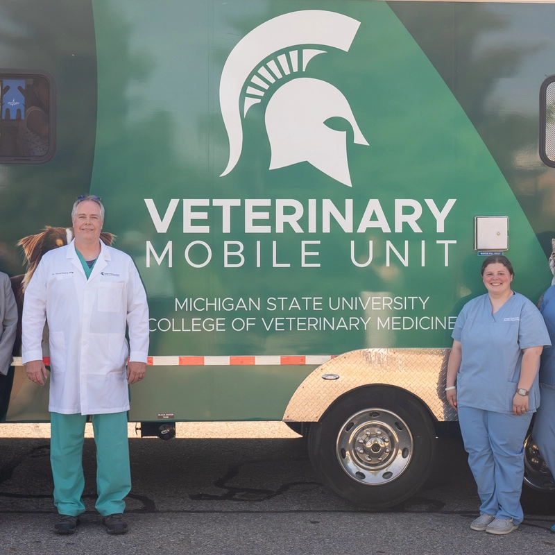 MSU College of Veterinary Medicine staff stand in front of the green Veterinary Mobile Unit trailer, decorated with a Spartan helmet and dog illustrations.