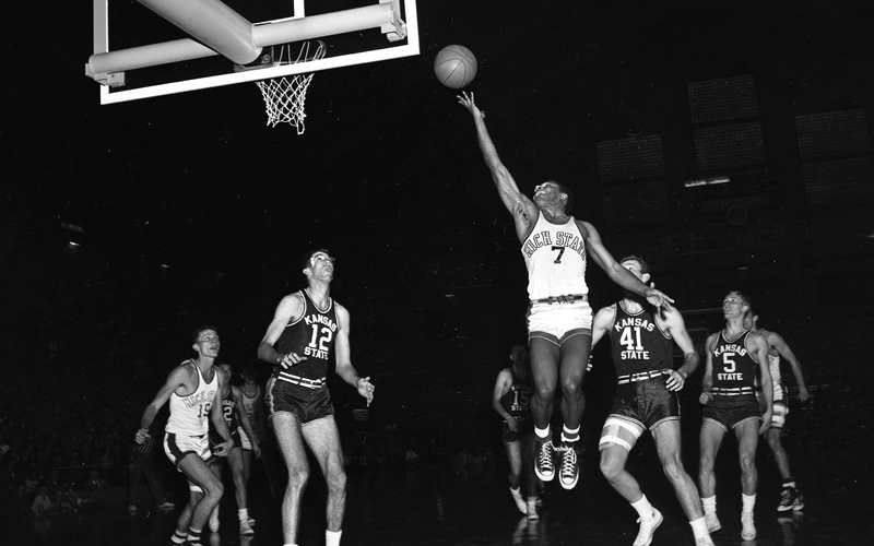 A Michigan State University basketball player shoots a layup against Kansas State in a black and white image from 1952