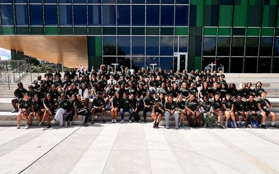 A group of students in black tee shirts pose in front of the Multicultural Center at Michigan State University