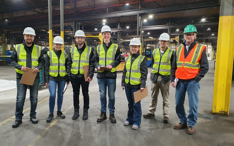 A group of people wearing neon vests and hard hats in an industrial setting.