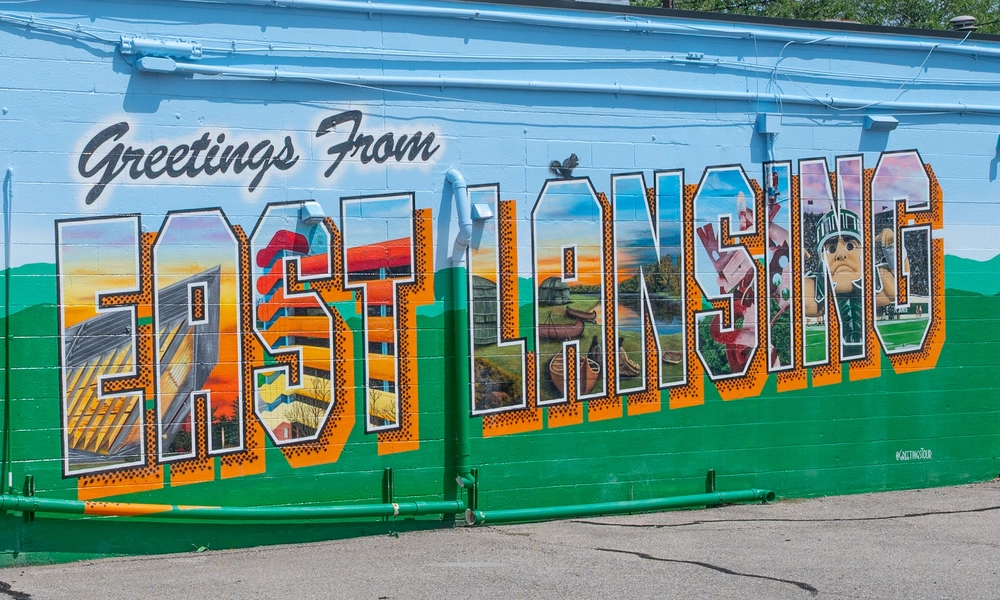 Mural on a brick wall that reads "Greetings From EAST LANSING" ... the East Lansing is filled with landmarks in East Lansing like the parking garage, the river trail, sparty and the Broad Art Museum