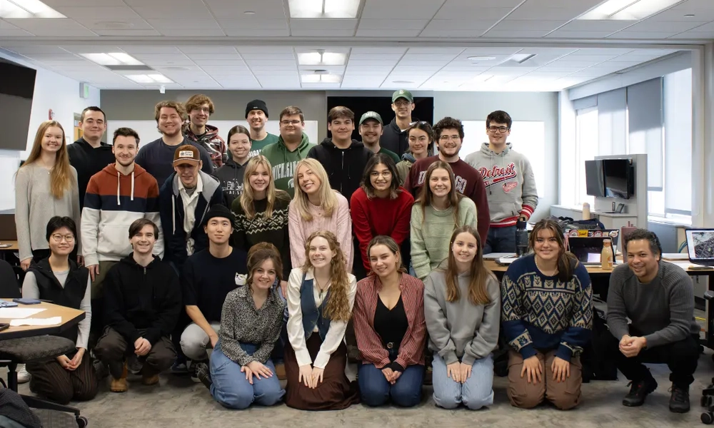 A group of people pose in a classroom in three rows