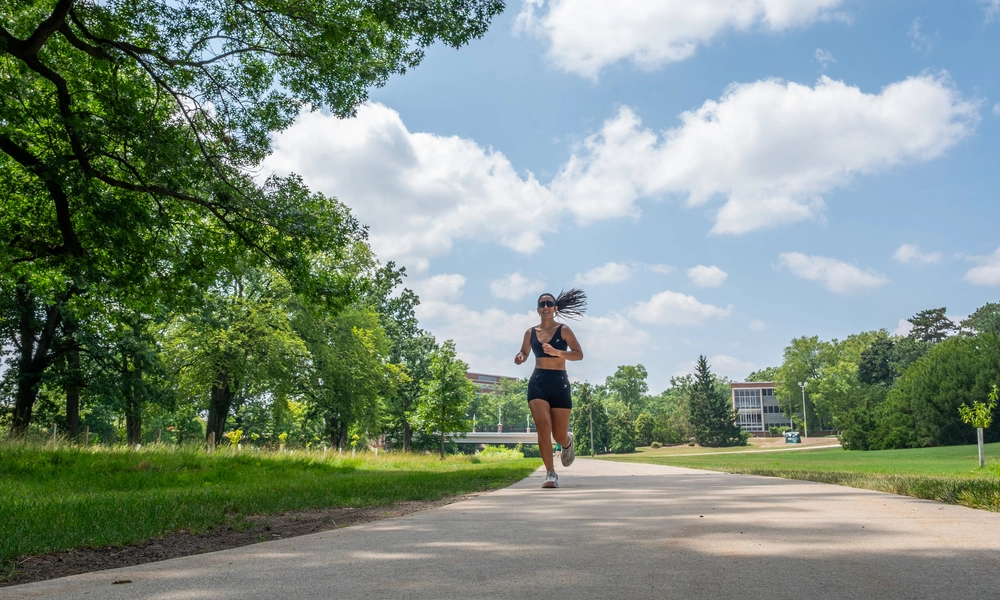 A runner jogs along a river trail on a partly cloudy day