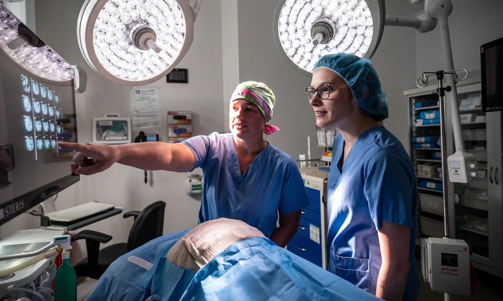 Two people in medical scrubs look at an x-ray image in a medical setting