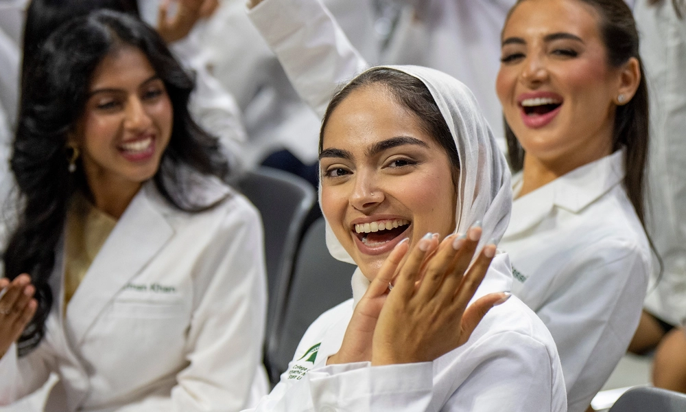 Smiling College of Osteopathic Medicine medical students in white coats clap and celebrate during Michigan State University’s White Coat Ceremony, marking the start of their journey as future physicians.