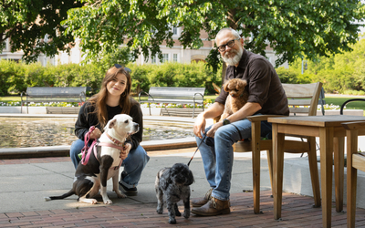 A man and woman posed outside with three dogs.