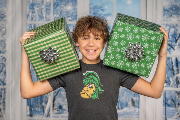 Smiling boy with wrapped gifts on either shoulder in front of a winter backdrop
