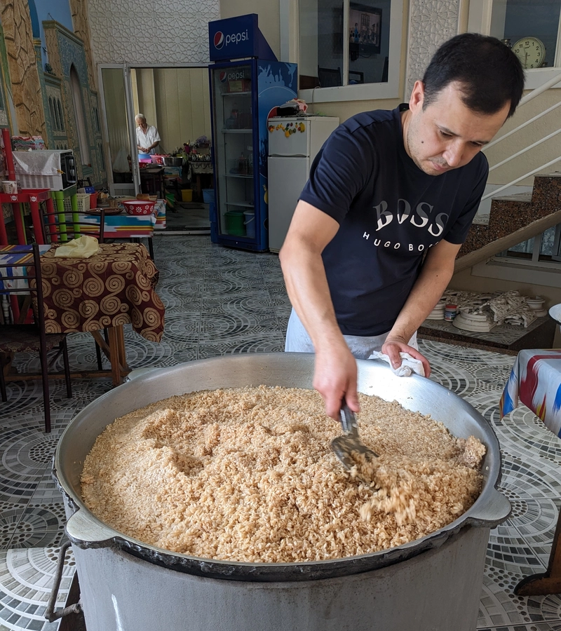 Man stirring a large pot of plov, rice pilaf.