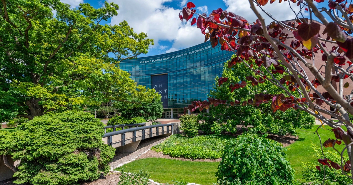 Clifton and Dolores Wharton Center for the Performing Arts seen behind green trees and flowers.