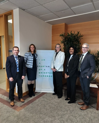 A group of five people stand together in an MSU College of Law lobby beside a banner that reads “I am a Spartan of a brighter tomorrow.”