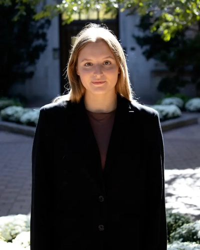 Grace Fitzgerald standing outdoors in sunlight wearing a dark blazer, facing the camera.