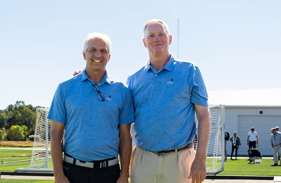 John Sorochan and John “Trey” Rogers III stand together on a field of grass.
