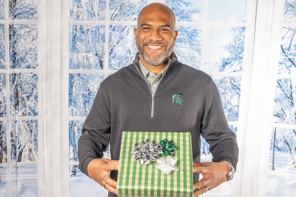 man smiling holding a wrapped gift in front of a winter backdrop