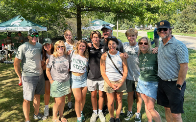 A group of people pose for a photo on MSU’s campus during a tailgate. They are all wearing green and white.