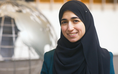 A woman in a black headscarf, MSU Assistant Professor Nareman Amin, stands by a globe sculpture in the MSU International Center in East Lansing, Michigan.