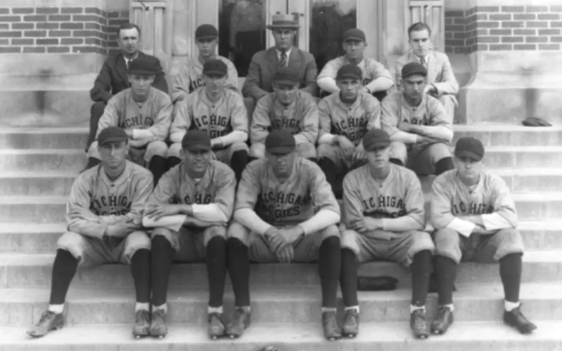Black and white photo of the 1925 Michigan State Baseball team. Players posed in their uniforms in three rows and catcher's gear in front of them. In the far right on the second row is Perry Fremont, who may have created the nickname the Spartans for MSU