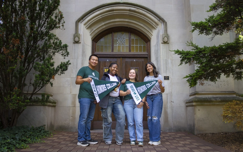 Four Honors College students hold green pennants outside Beaumont Tower at MSU.