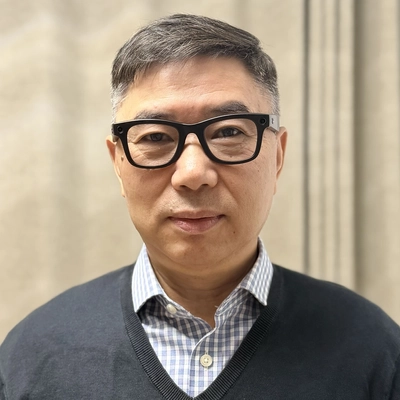 Shi-you Ding poses for a portrait wearing glasses, a button-down shirt and a sweater
