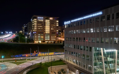 Two buildings on either side of a road with lights on against the night sky.