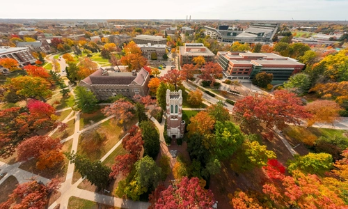 Aerial view Beaumont Tower surrounded by colorful fall foliage as pathways wind through grassy areas and trees