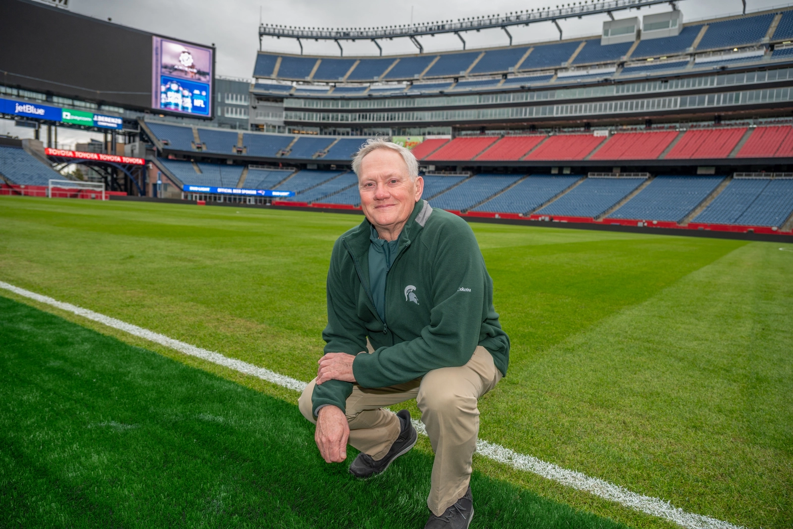 John 'Trey' Rogers III kneels on the natural-grass field at Gillette Stadium outside Boston, one of the temporary-field venues prepared for the 2026 World Cup.